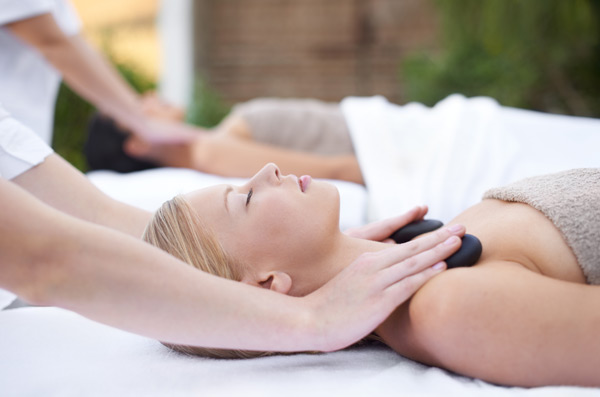 Massage therapy with stones, two woman receiving massage from two therapist