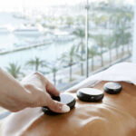 Hand placing hot stone on a client chakras for professional massage and yachting background