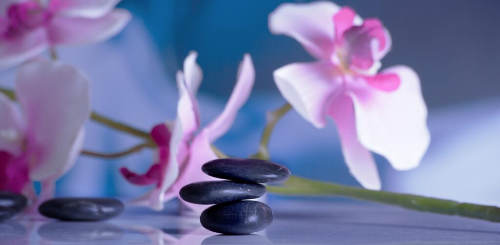 Spa hot stones with pink orchids creating a calming massage setting for body massage oil and wellbeing