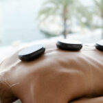 Hot stone massage therapy, blue backgoud with palmers inviting a relaxing athmosphere for different types of massages