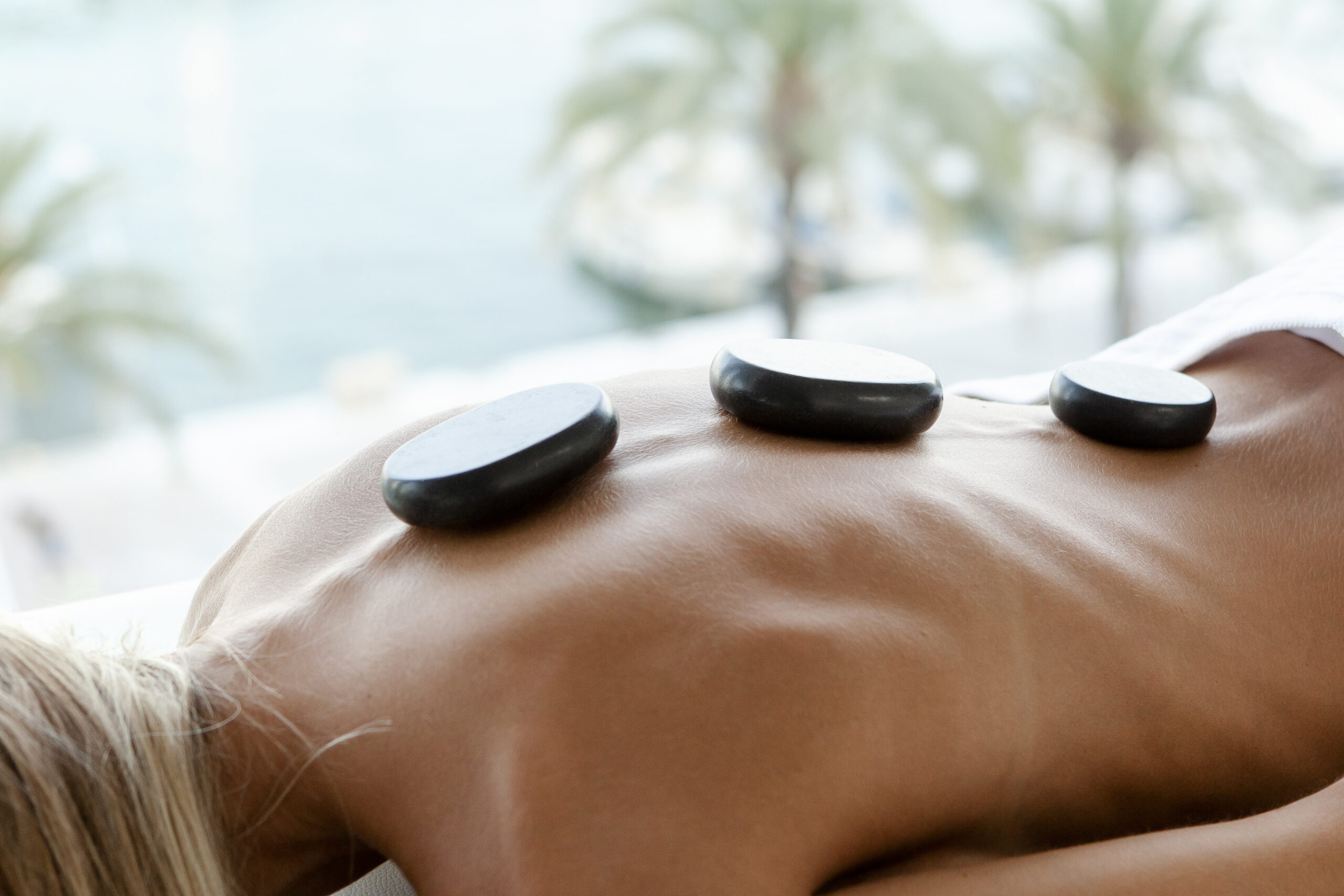 Hot stone massage therapy, blue backgoud with palmers inviting a relaxing athmosphere for different types of massages