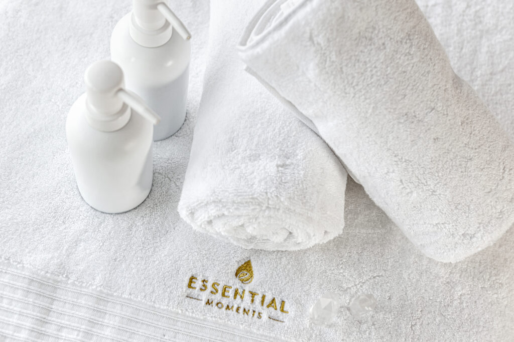Profesional massage setup with 2 white towels and 2 white oil bottles for massage with Essential-Moments logo on.
