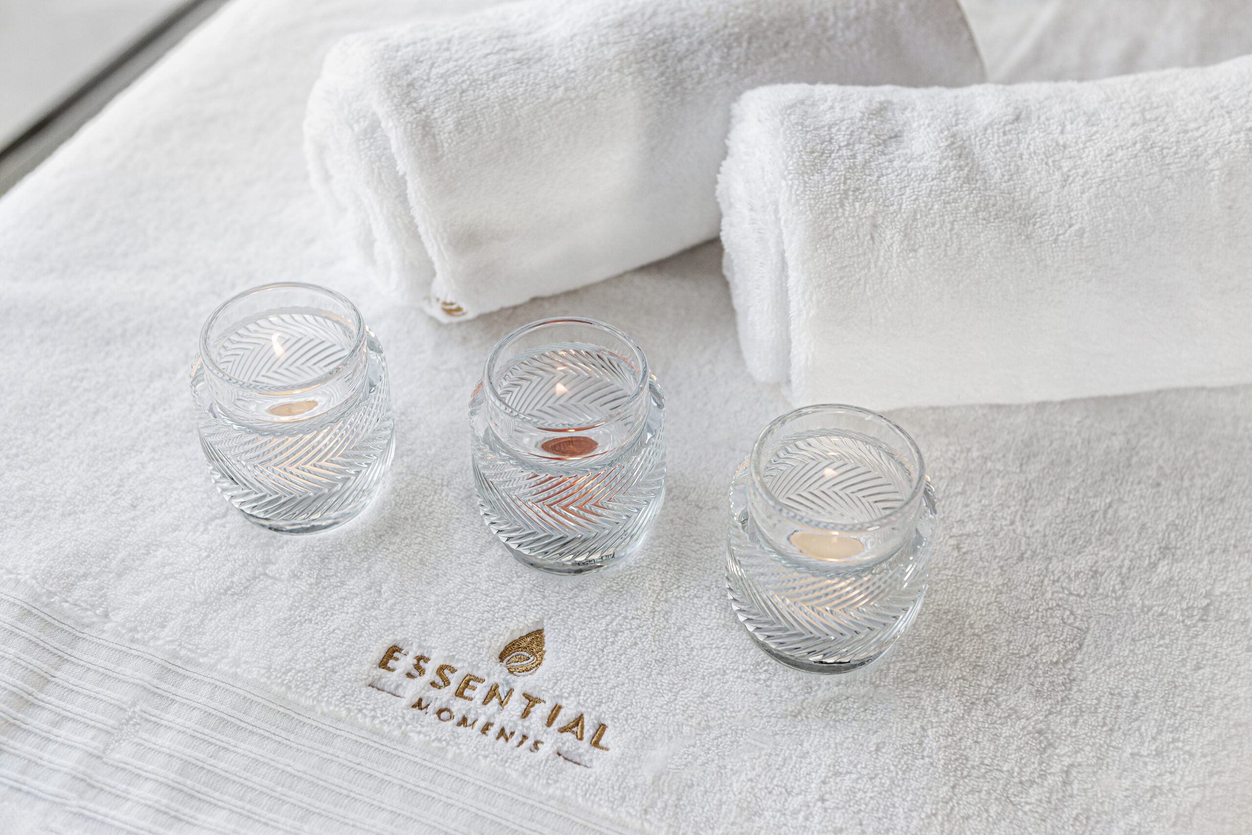Massage setup with three candels and two white towels with Essential-Moments logo on.