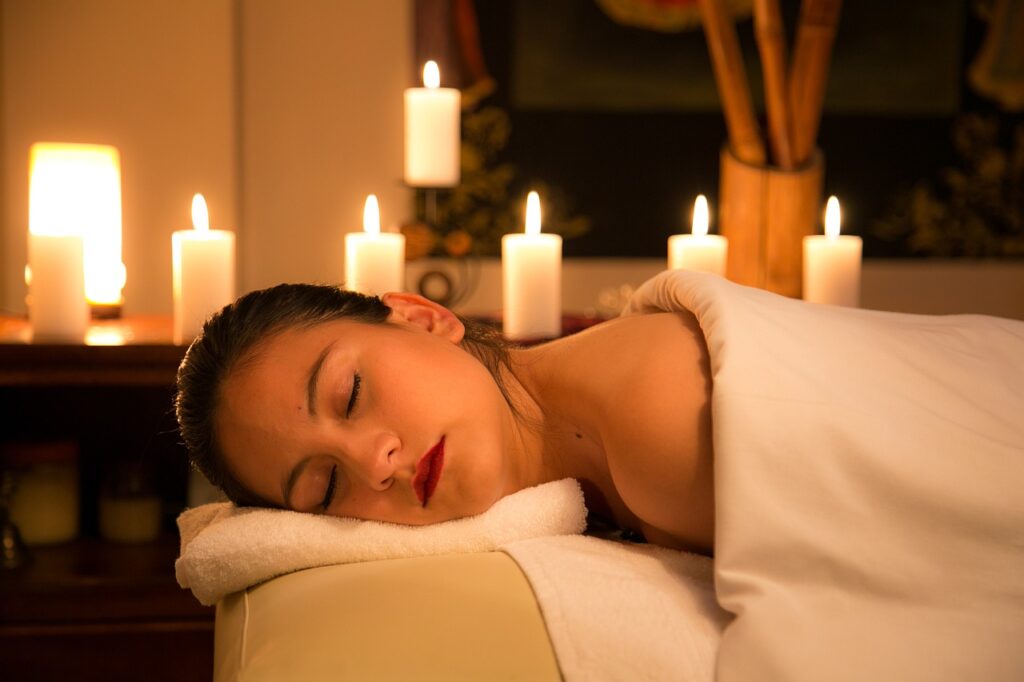 Client prepared for a massage treatment on a  massage bed covered by white towels towels and white candles around.