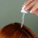 Lady with red hair applyng serum on scalp, preparation for head massage