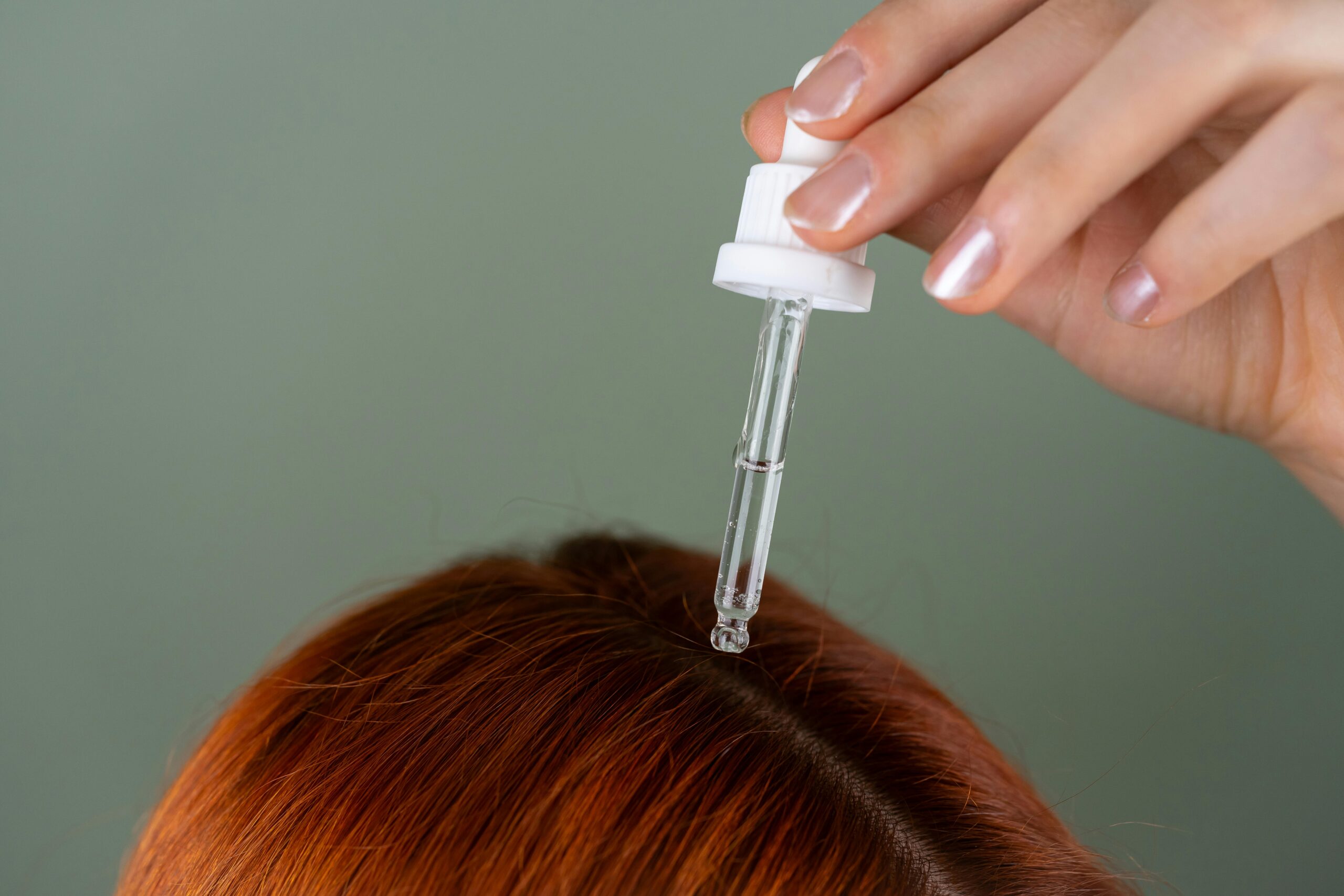 Lady with red hair applyng serum on scalp, preparation for head massage