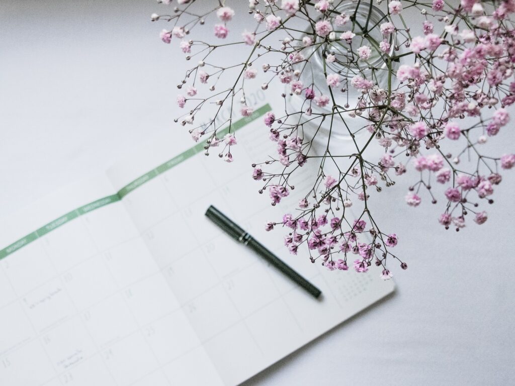 Schedulle for massage, book, pen and pink flowers on top