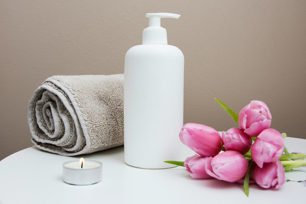 Premium massage experience, towel, white oil bottle , candle and pink flowers