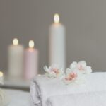 Relaxing massage therapy setting with white towels, white flowers and candles in a spa treatment room