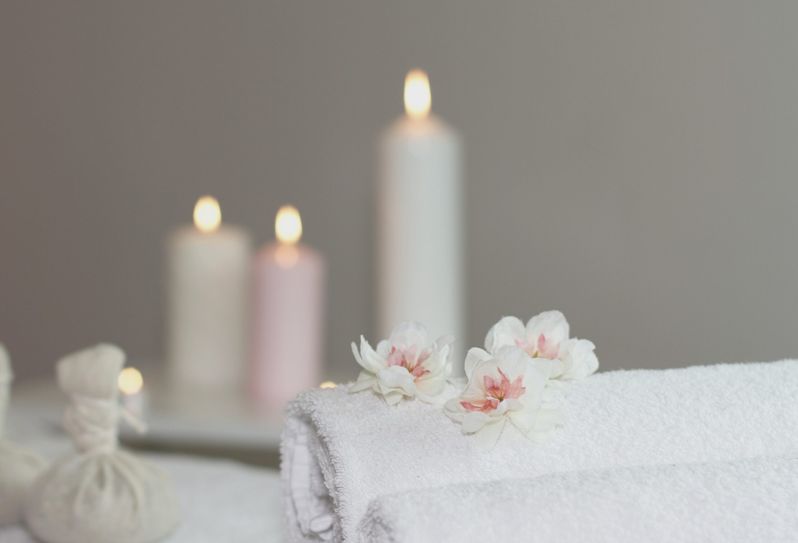 Relaxing massage therapy setting with white towels, white flowers and candles in a spa treatment room