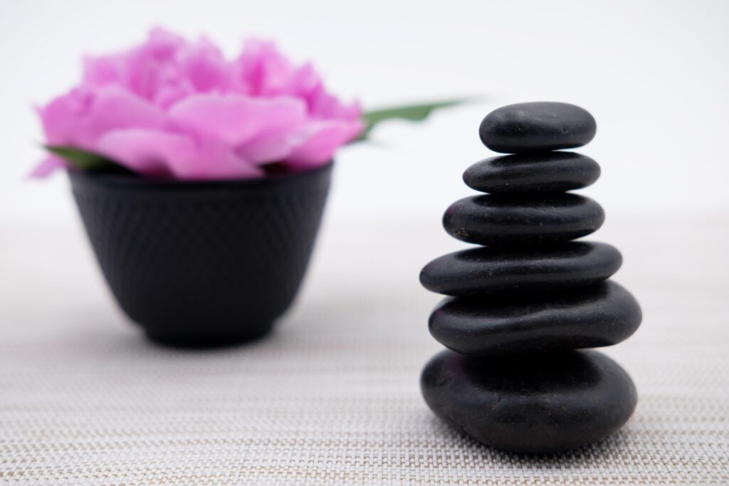 Hot Stone Massage therapy set- up with black volcanic stones and a bole with pink rose petals